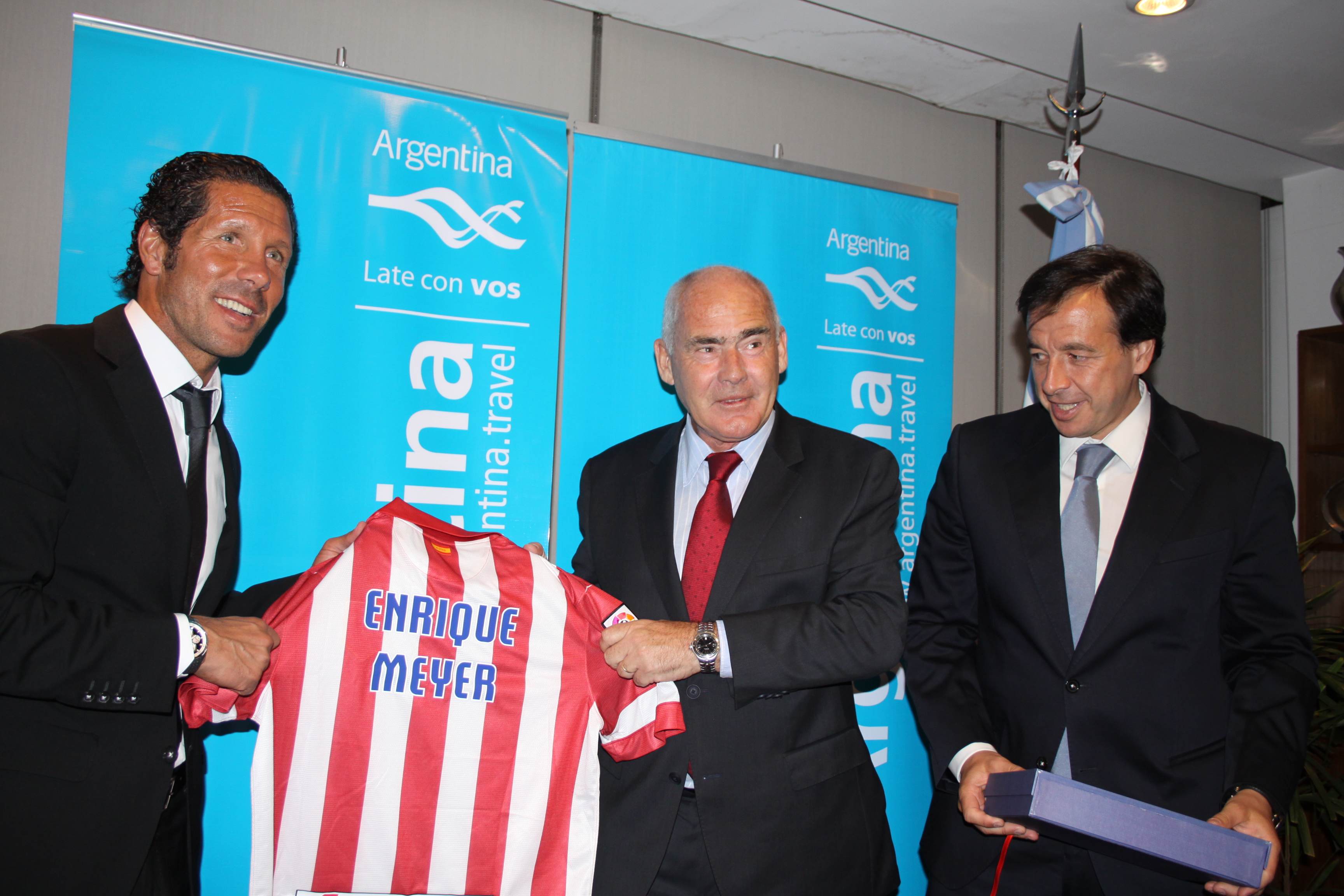 El director Técnico del Atlético Madrid, Diego Simeone, entrega la camiseta del club al ministro de Turismo de la Nación, Enrique Meyer, junto al vicepresidente de la institución española, Antonio Alonso.